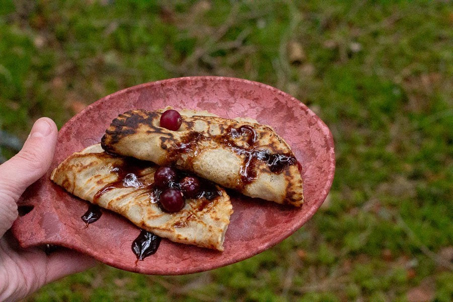 Roter Kupilka 14 Small Teller mit Pfannkuchen und Kirschen, in der Hand über dem Gras