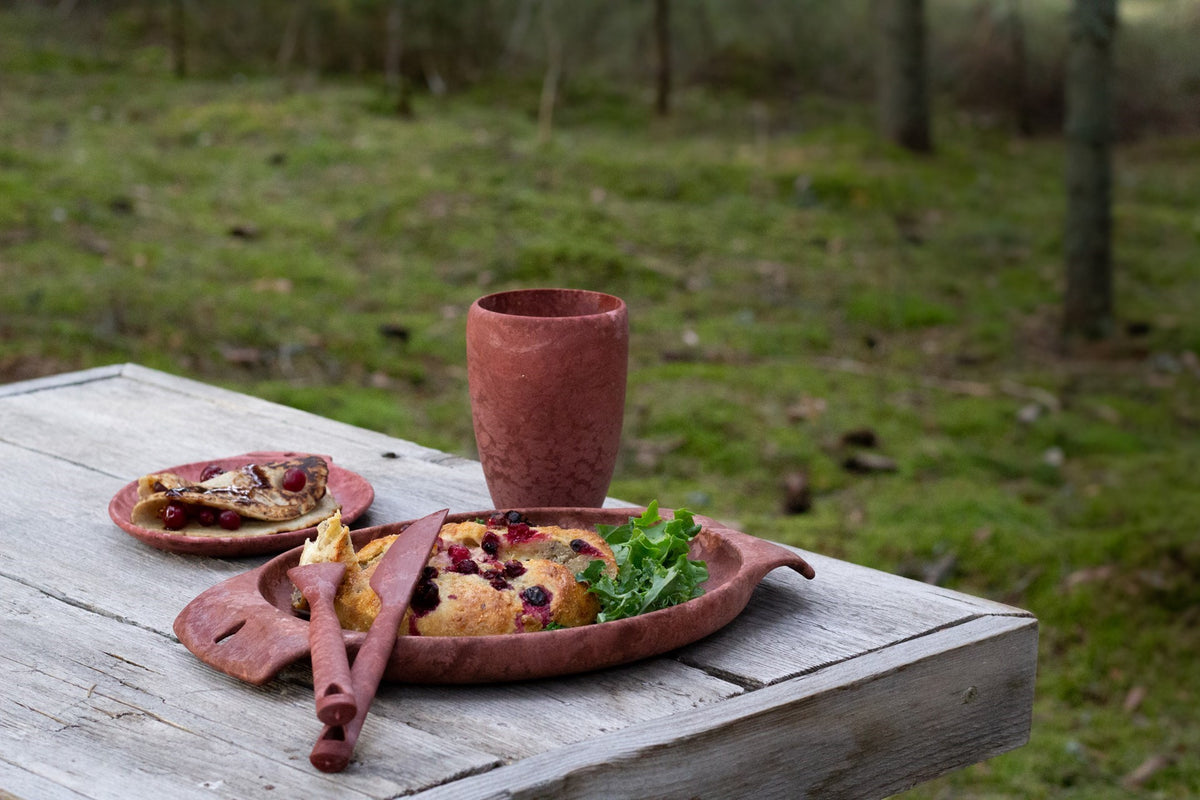 Rote Kupilka 30 Coffee Go Cup auf einem Holztisch im Freien neben roten Tellern mit Essen