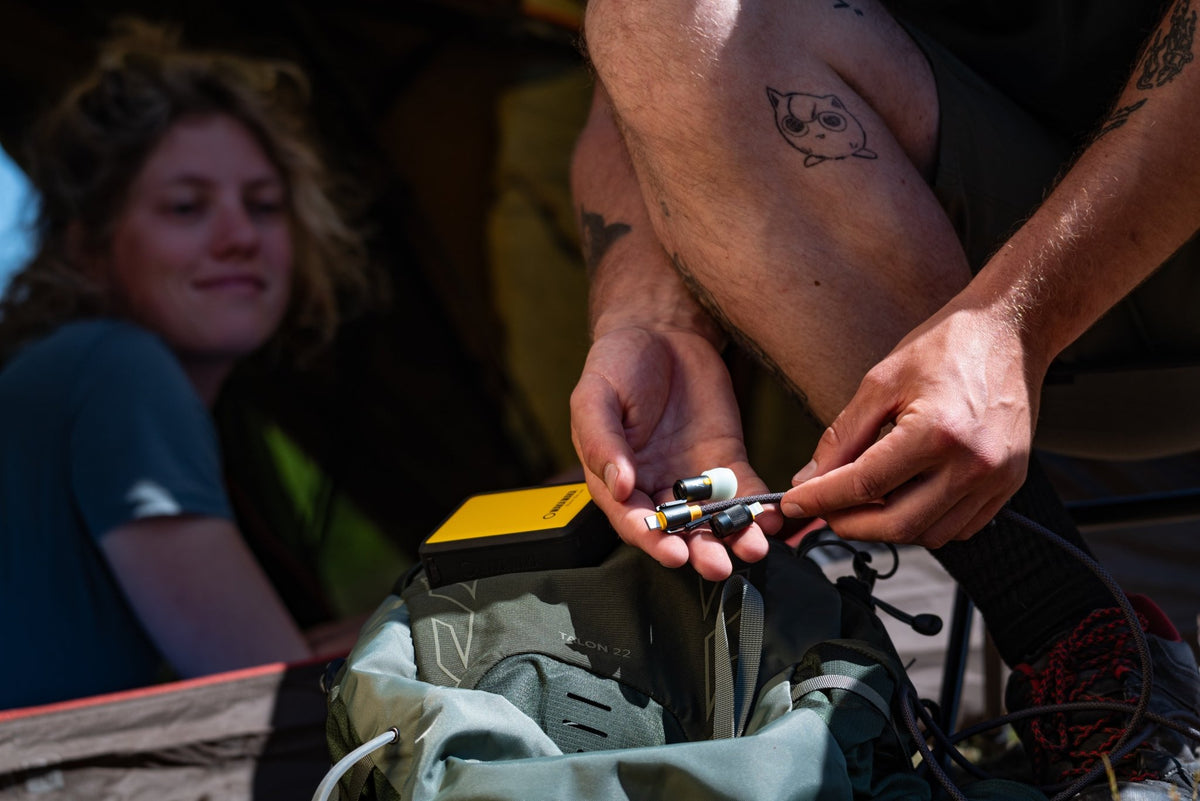 WakaWaka Connect Pro wird draußen an eine gelbe Powerbank über einem Rucksack angeschlossen