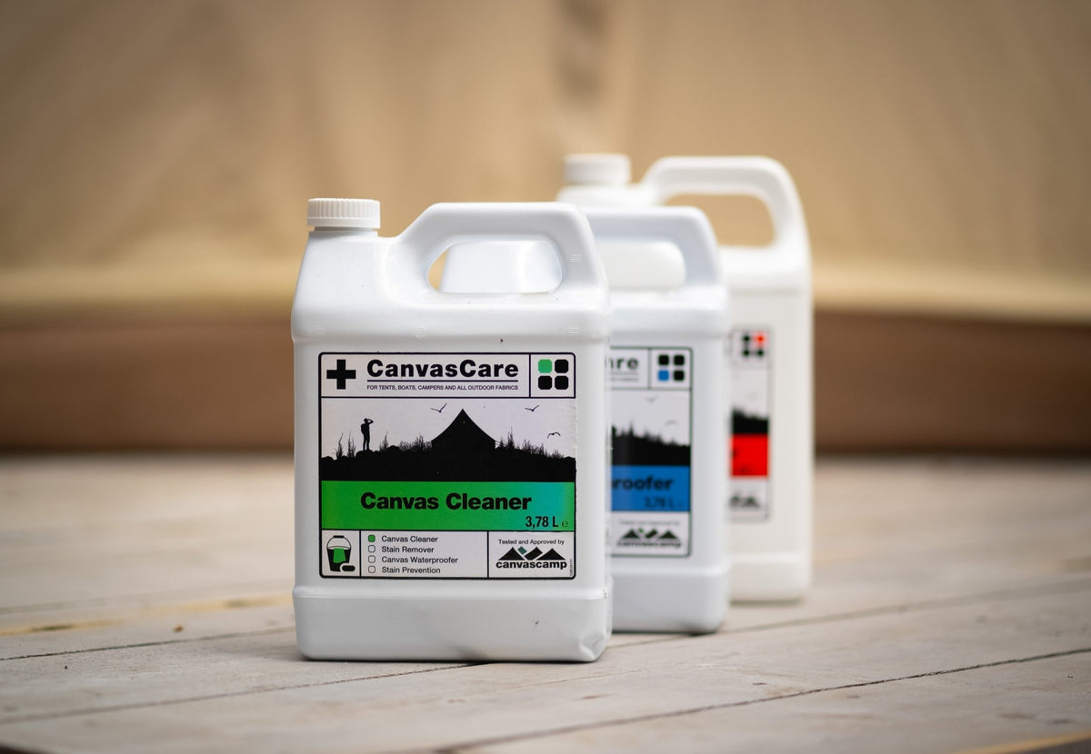 CanvasCare Canvasreiniger vorne auf einem Holzboden, dahinter Flaschen mit blauem und rotem Etikett