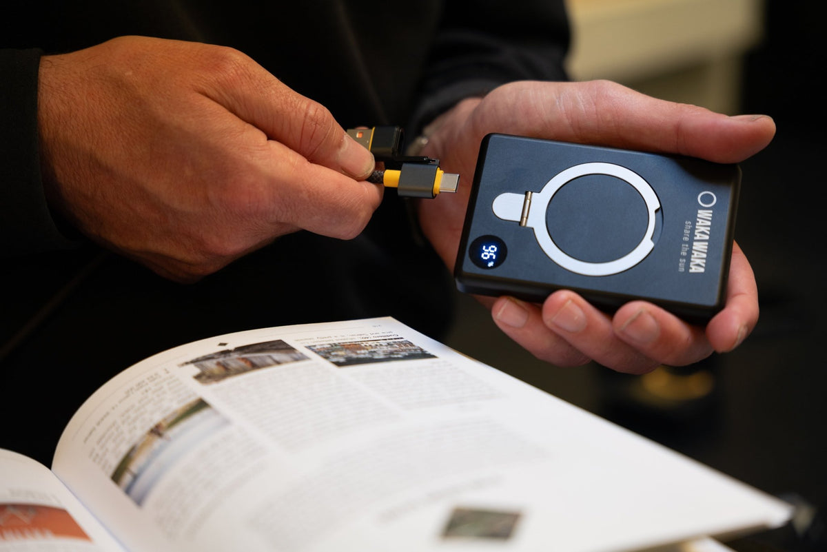 WakaWaka Power Pro in Schwarz in der Hand, während ein Kabel angeschlossen wird, über einem Buch