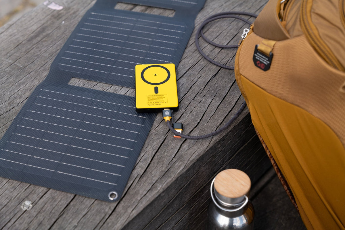 WakaWaka Power Pro in Gelb auf einem faltbaren Solarpanel auf einer Holzbank neben einer Tasche