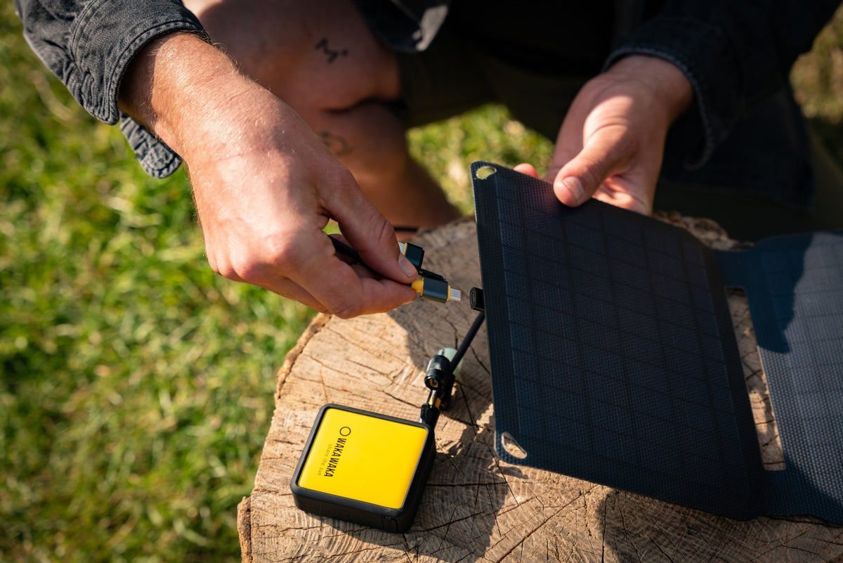 WakaWaka Solar 10 auf einem Baumstumpf im Gras, an eine gelbe Powerbank angeschlossen