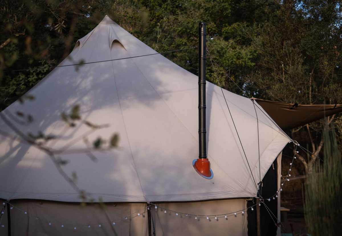 CanvasCamp Exit 45° auf einem hellen Glockenzelt mit Lichterkette, Ofenrohr durch das Zeltdach