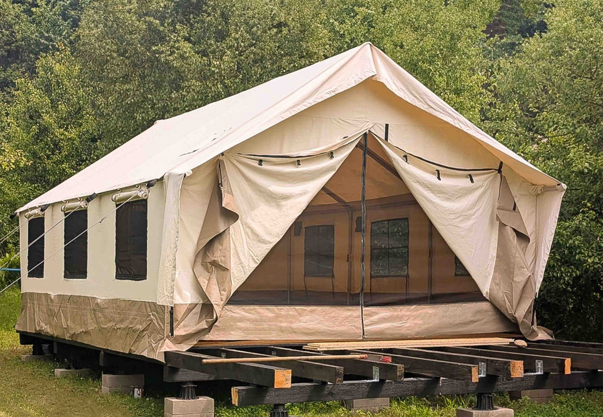 CanvasCamp Heavy Duty Safari Tent auf einer Holzplattform zwischen Bäumen mit offener Tür