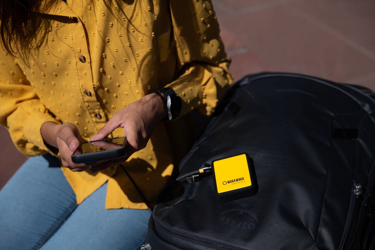 WakaWaka Power 20 auf einem schwarzen Rucksack, mit einem Kabel zum Handy einer Frau