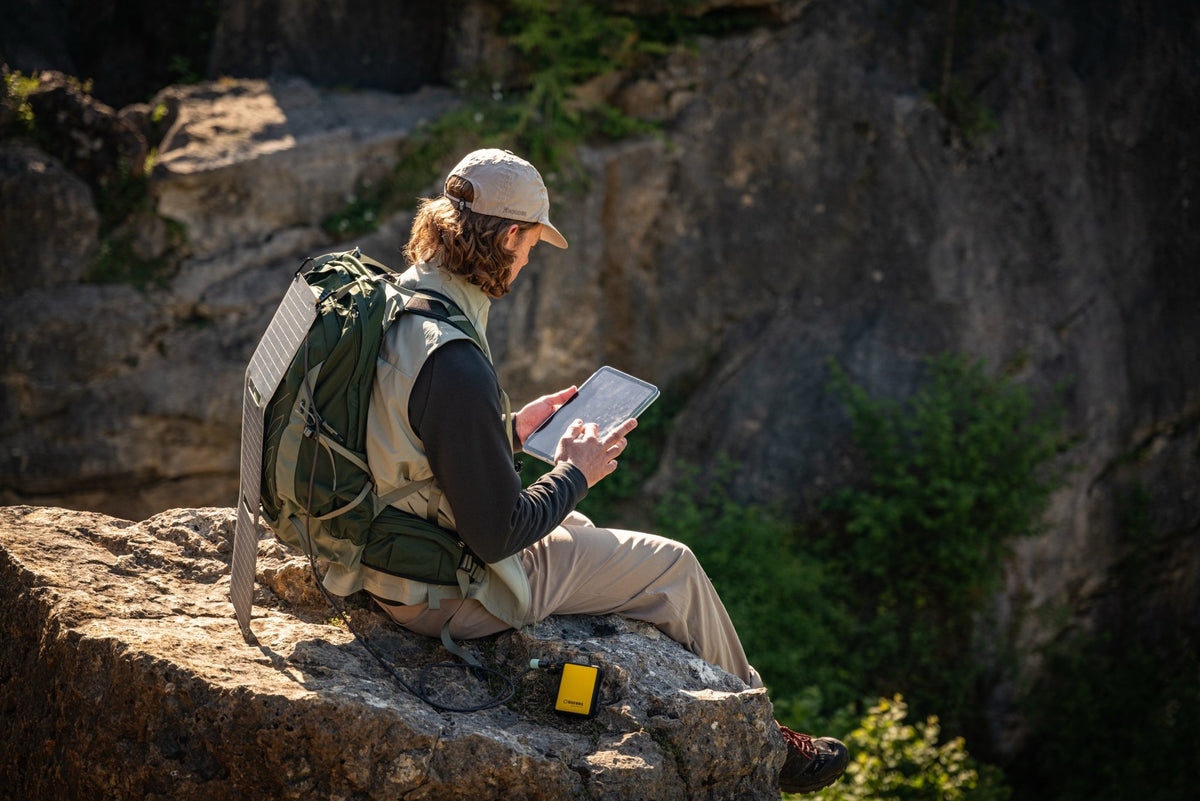 WakaWaka Power 20 auf einem Felsen neben einem Wanderer mit Rucksack, der ein Tablet benutzt