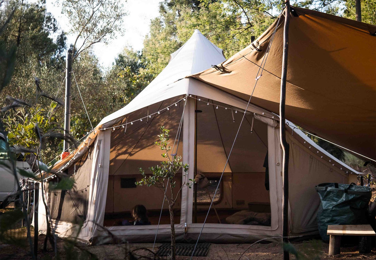CanvasCamp Sibley Apex 520 Panorama mit offener Front, Lichterkette und Tarp zwischen den Bäumen