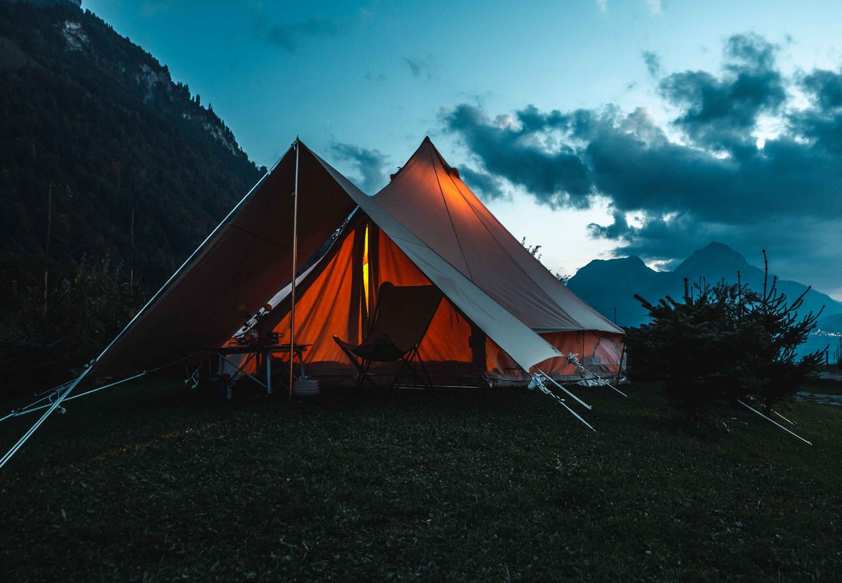CanvasCamp Sibley Bell Tent Connector zwischen zwei beleuchteten Glockenzelten am Abend nahe den Bergen