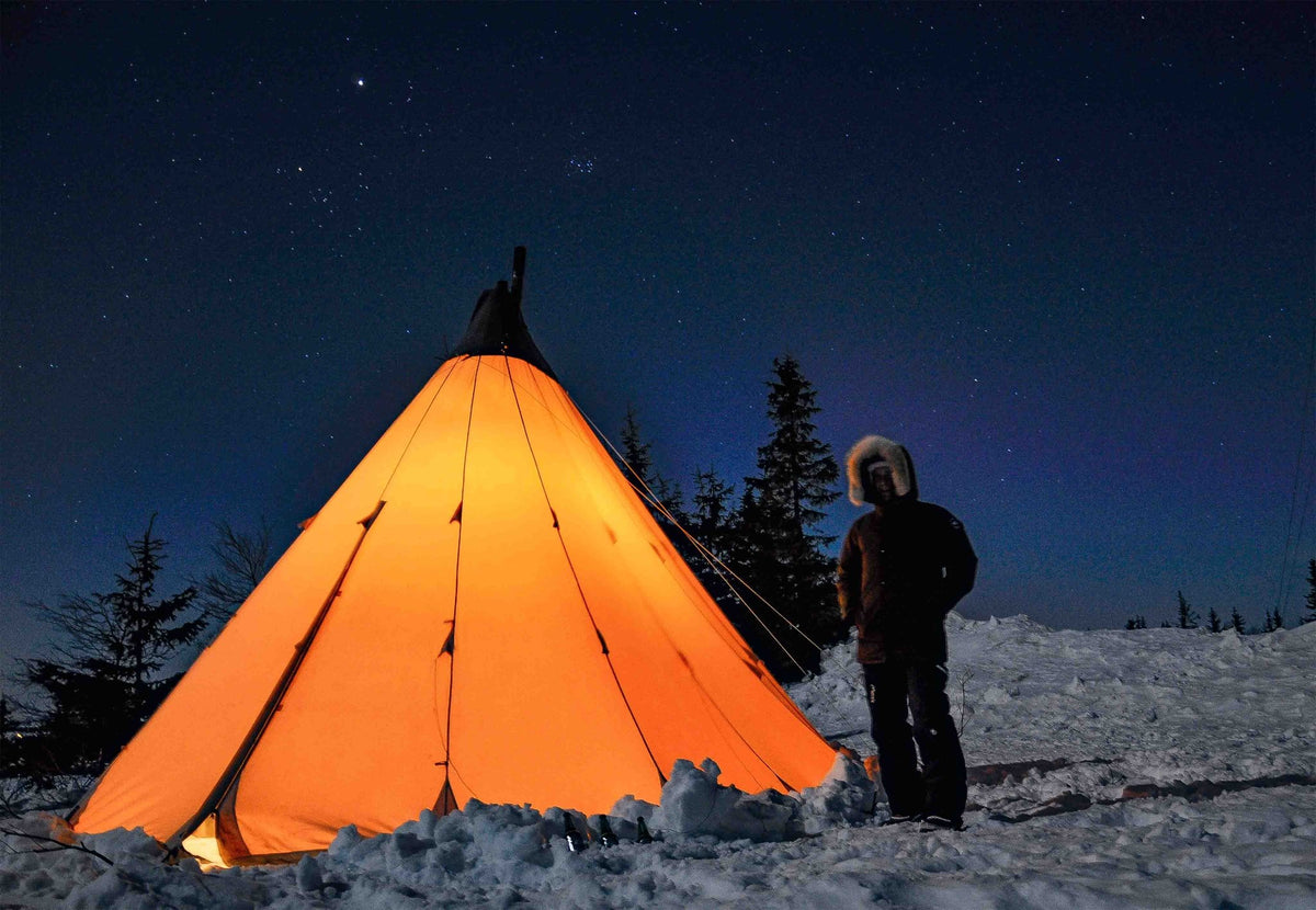 CanvasCamp Traveller 400 beleuchtet im Schnee bei Nacht mit einer Person daneben