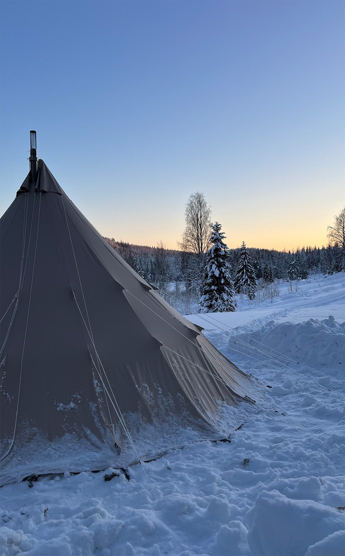 CanvasCamp Traveller 500 im Schnee bei Sonnenuntergang mit Ofenrohr durch die Spitze