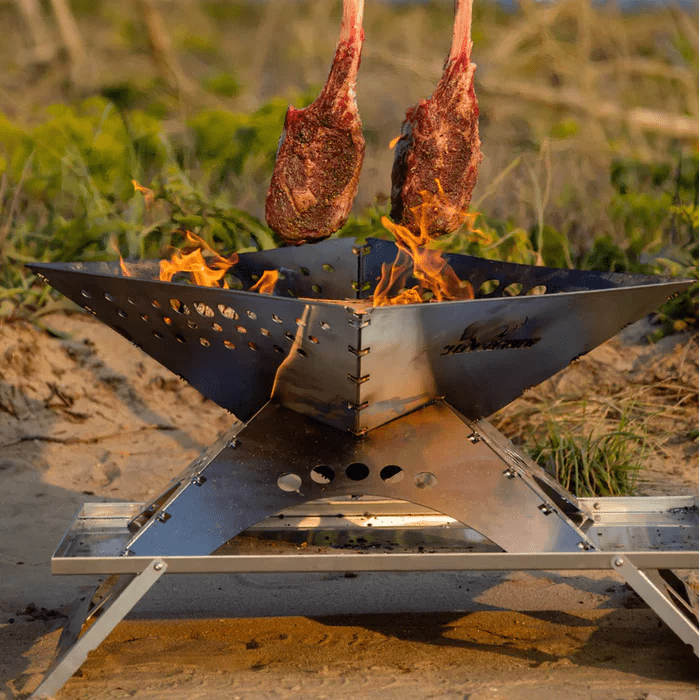 Winnerwell Zubehörtisch an einer brennenden flachen Feuerschale mit Fleisch über dem Feuer