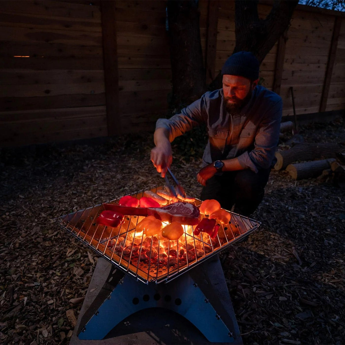 Winnerwell Bratrost auf einer brennenden flachen Feuerschale mit Fleisch und Gemüse am Abend