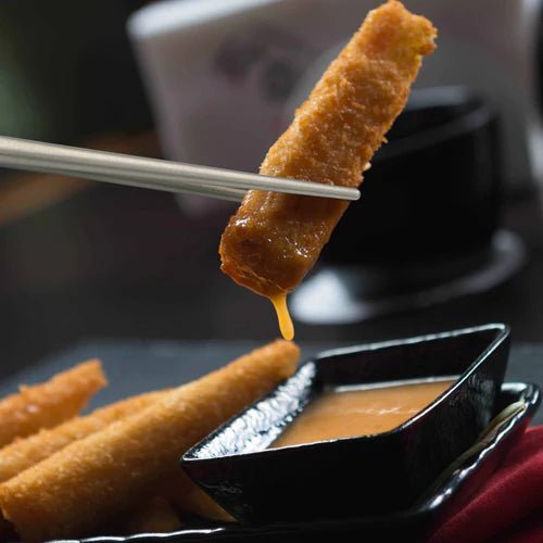 Winnerwell Essstäbchen greifen einen frittierten Snack über einem Schälchen Soße