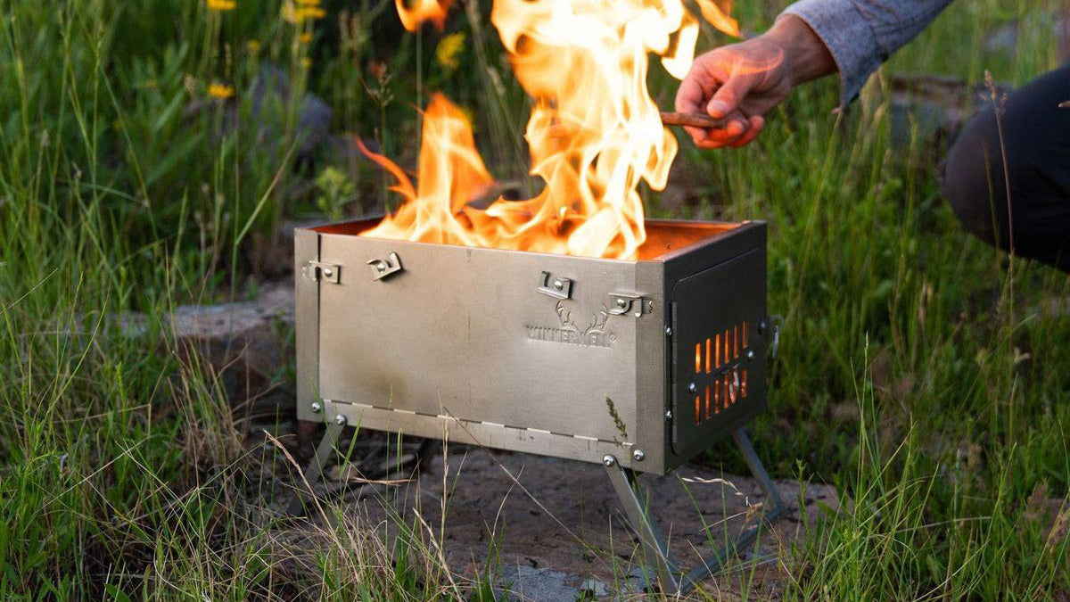 Outdoor-Kamine, Feuerschale aus Stahl auf kleinen Füßen mit brennendem Holz im Gras