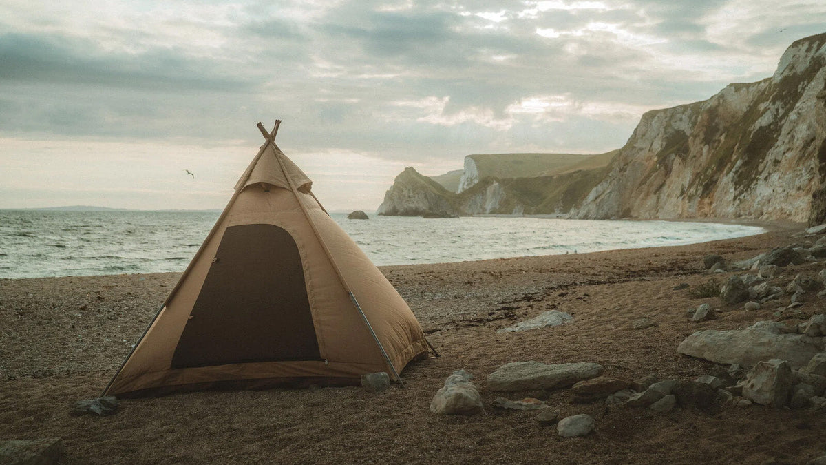 Zelte, beiges Tipi Zelt mit offener Tür an einem Kieselstrand am Meer vor weißen Klippen