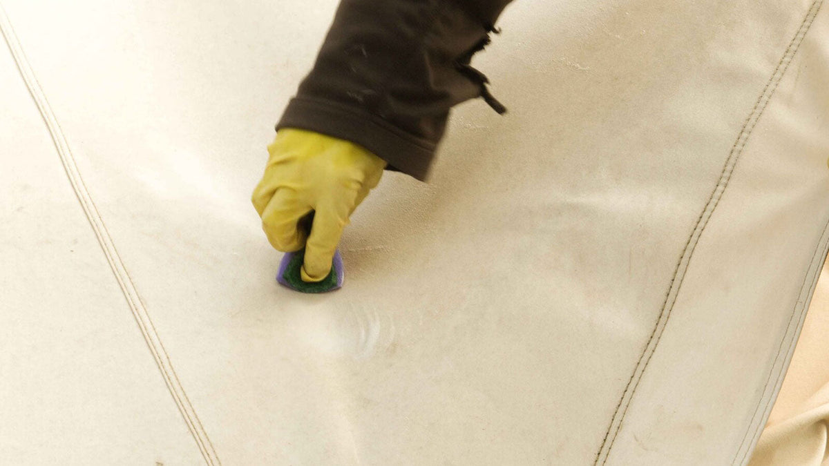 Textil- und Polsterreiniger, Hand in gelbem Handschuh putzt eine Stelle auf weißem Zeltstoff