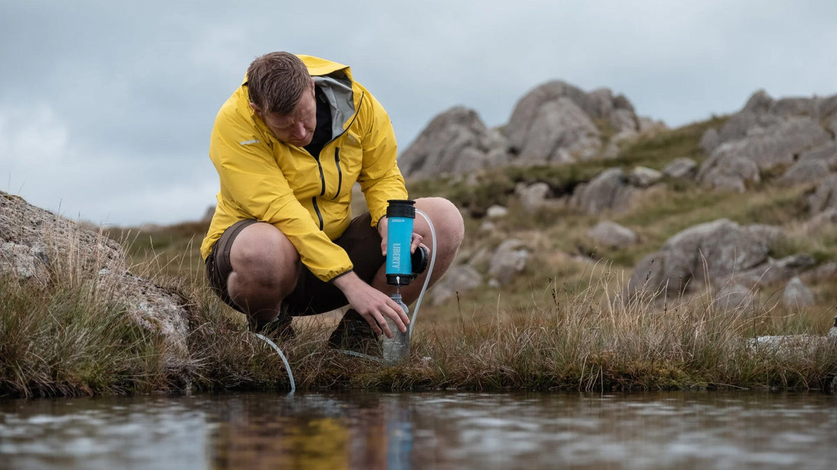 Tragbare Wasserfilter und Wasseraufbereiter, Wanderer filtert Bachwasser in eine blaue Flasche