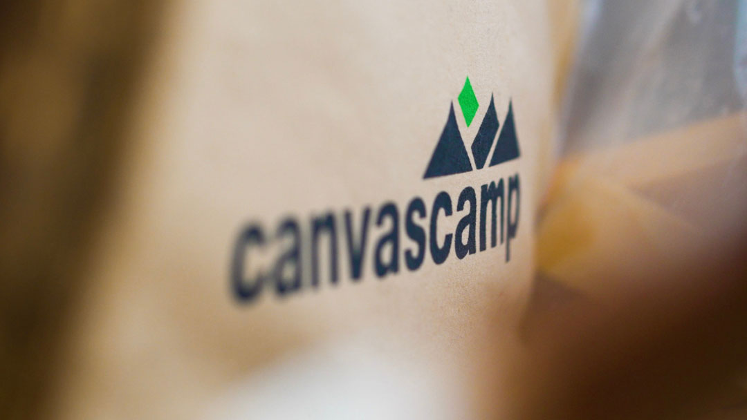 Gruppenzelte, CanvasCamp Logo mit Bergen und einer grünen Raute auf beigem Zeltstoff