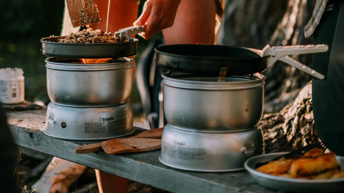 Kochen und Topfsets, zwei Campingkocher mit Töpfen und Pfannen auf einer Holzbank