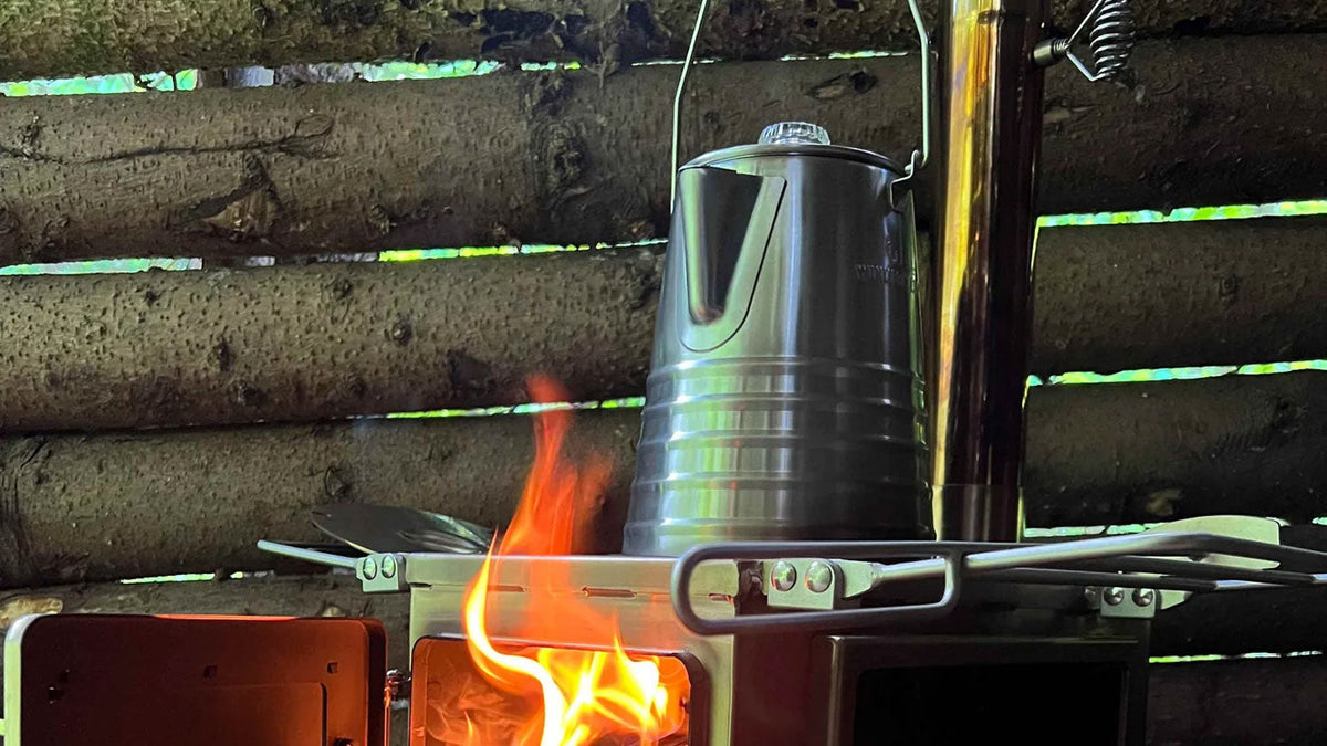 Perkolatoren, Perkolator aus Stahl auf einem Ofen mit offenem Feuer in einer Blockhütte