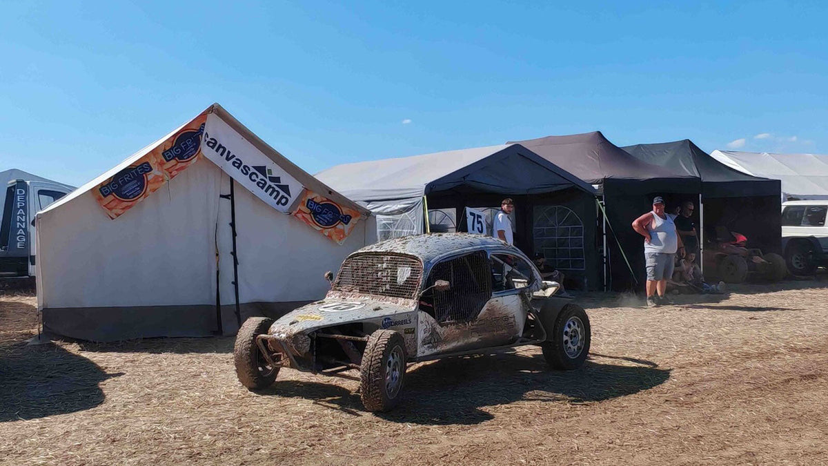 Safarizelte, weißes Zelt mit Banner neben einem schlammigen Buggy auf staubigem Gelände