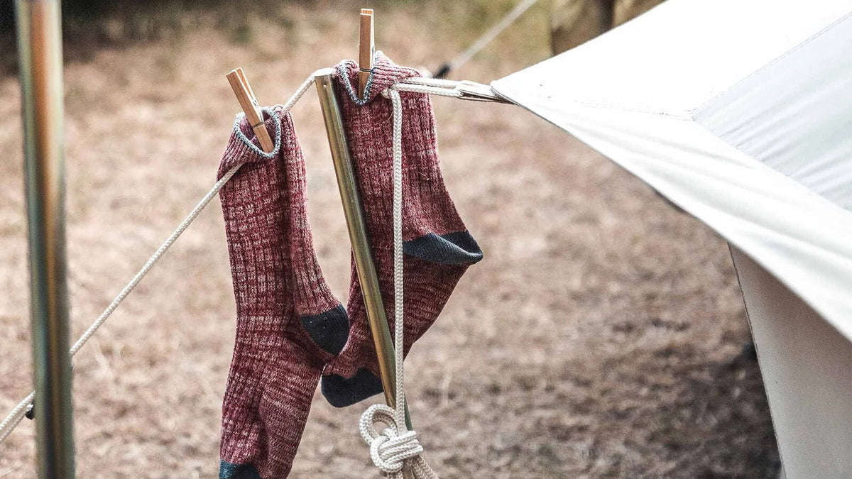 Zeltstangen, rote Wollsocken mit Wäscheklammern an einer Leine bei einer Zeltstange aus Holz und einem Tarp