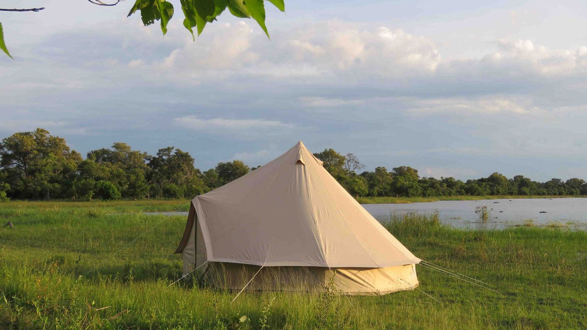 CanvasCamp Traveller, beiges Glockenzelt auf einer Wiese an einem See mit Bäumen