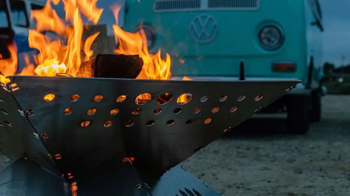 Feuerschalen, brennendes Holz in einer gelochten Feuerschale aus Metall, mit einem mintgrünen Volkswagen Bus dahinter