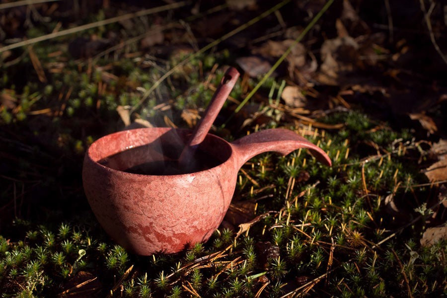 Rote Kupilka 21 Classic Cup mit dampfendem Getränk und Löffel auf Moos in der Sonne