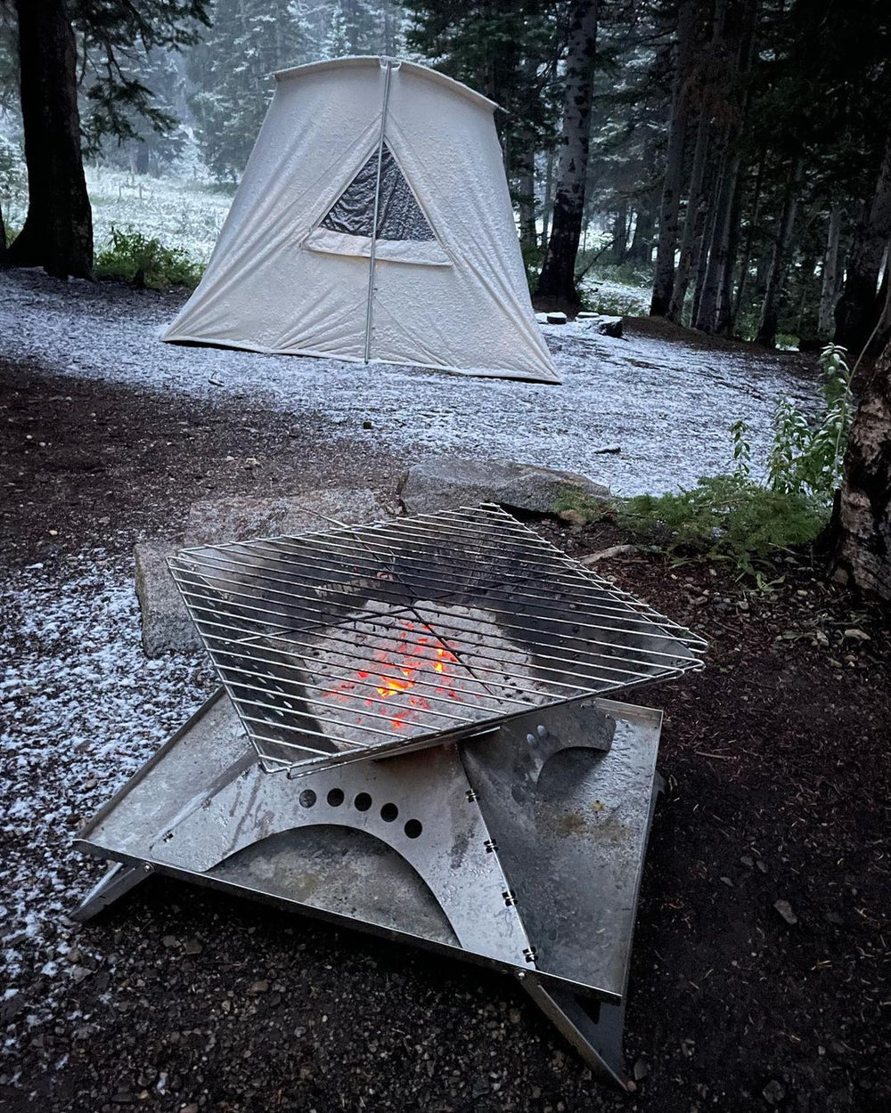 Winnerwell Flache Feuerschale mit Grillrost und glühender Kohle im Schnee vor einem Canvas-Zelt