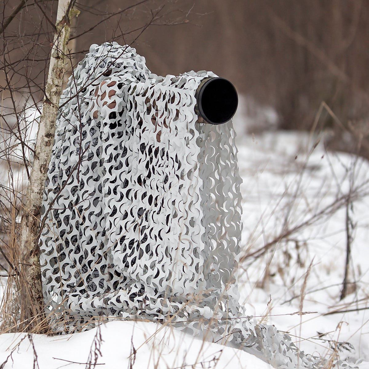 Buteo 3D Leafs Tarnnetz Schnee im Einsatz im Schnee, das Objektiv ragt rechts aus dem Netz