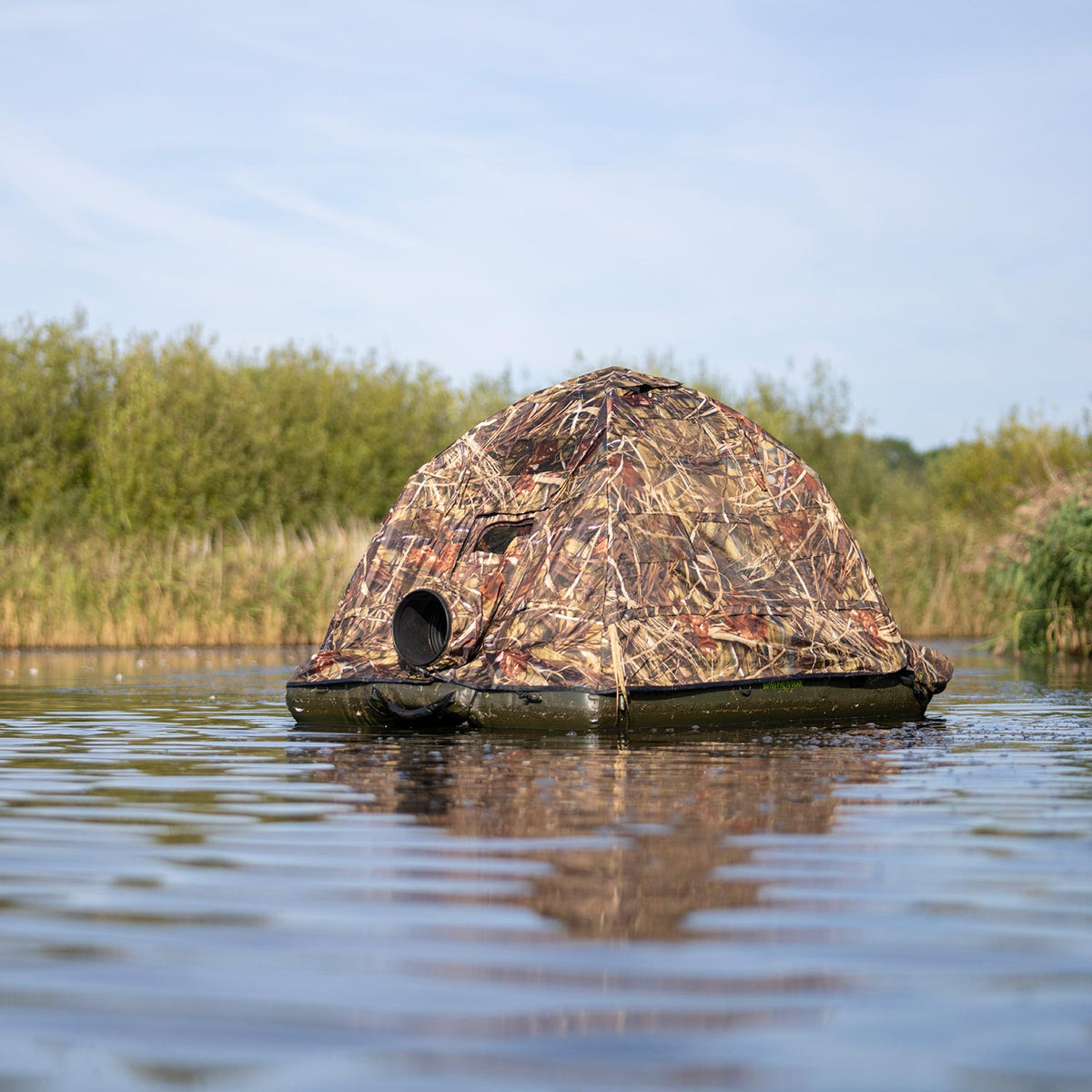 Buteo Schwimmtarnzelt Grebe direkt von vorn auf dem Wasser, runde Objektivöffnung und Schilf im Hintergrund