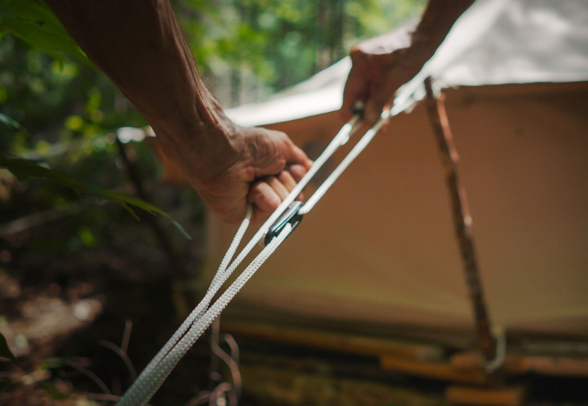 CanvasCamp Abspannleine mit Spanner, Hände ziehen die Leine neben dem Zelt straff