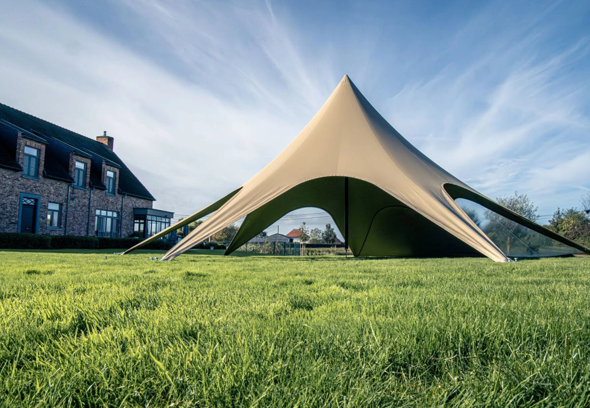 CanvasCamp StarShade Pro Eventzelt aus niedriger Perspektive vom Gras, mit einem Backsteinhaus dahinter