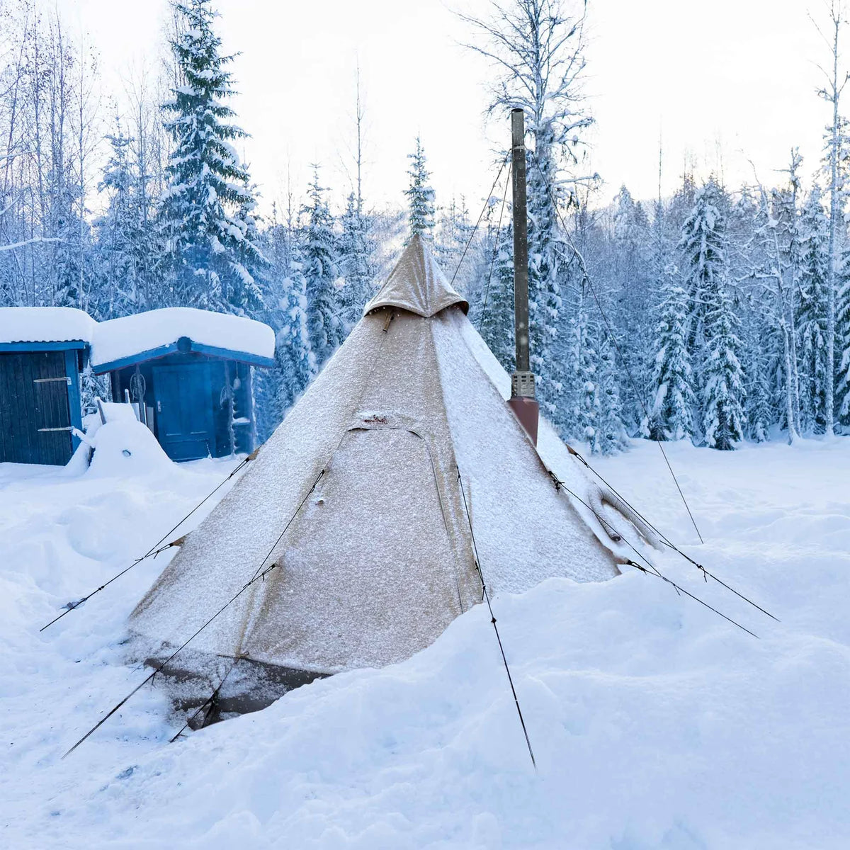 Winnerwell Arctic Tipi Zelt mit Rauchrohr im Schnee zwischen verschneiten Kiefern