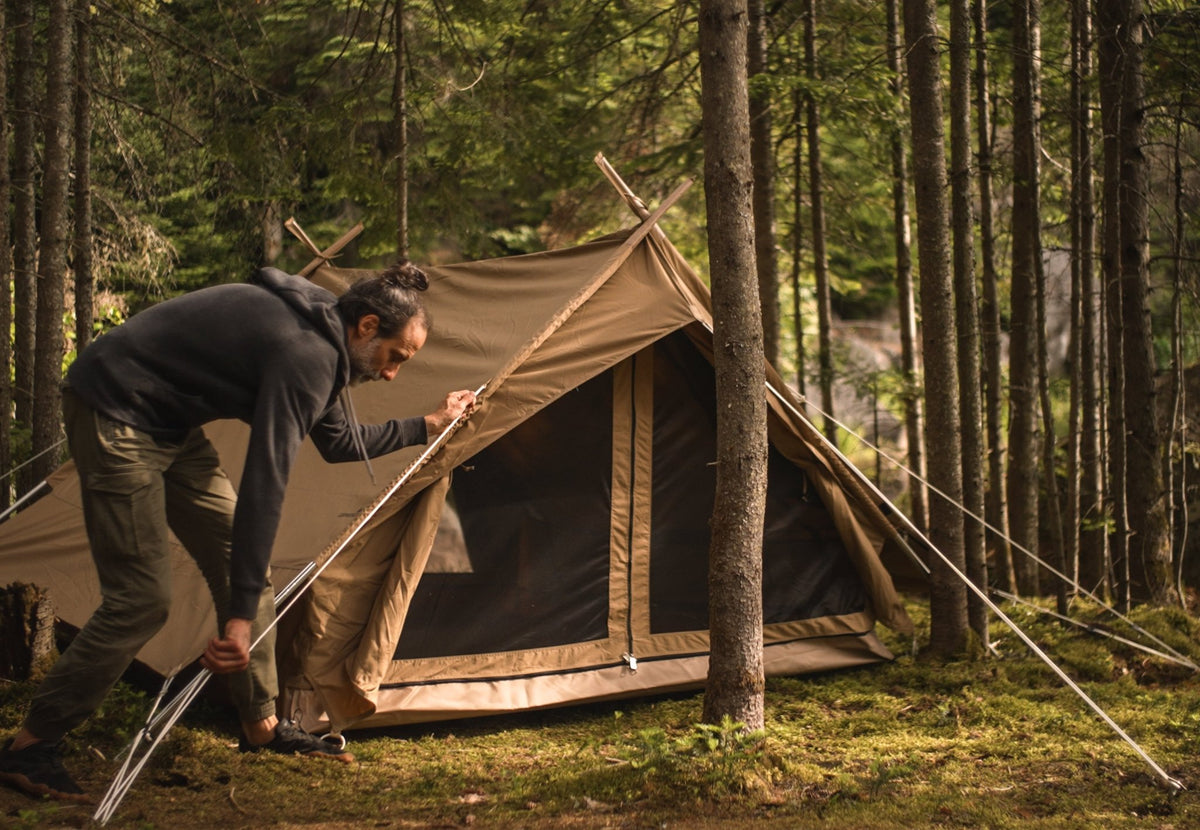 CanvasCamp Altaï wird im Wald von einem Mann aufgebaut, der die vordere Stange hält