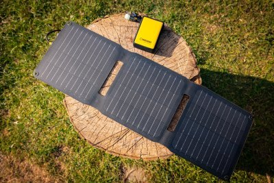 WakaWaka Solar 20 von oben auf einem Baumstumpf im Gras, mit einer gelben Powerbank