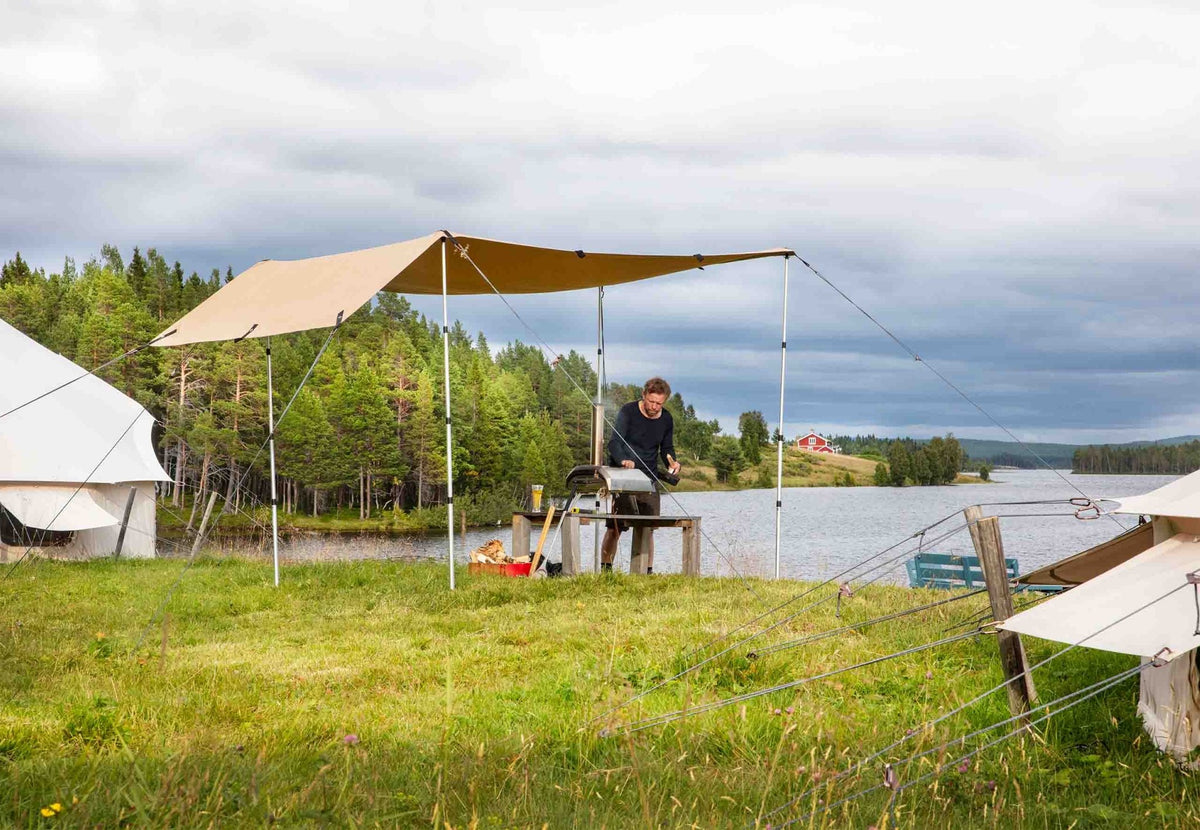 CanvasCamp Heavy Duty Shelter als Vordach am Wasser, mit einem Mann an einem Tisch darunter