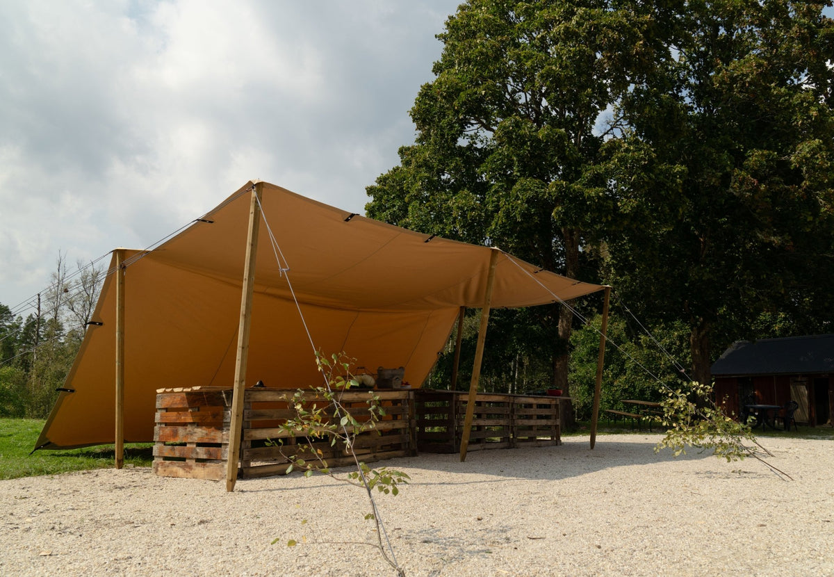 CanvasCamp Heavy Duty Shelter mit Holzstangen über einer Sitzecke auf Kies aufgebaut