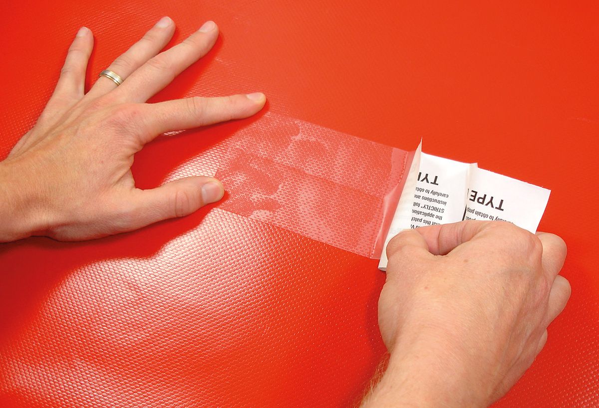Tear-Aid A durchsichtiger Reparaturstreifen wird von Hand auf rotes Material geklebt