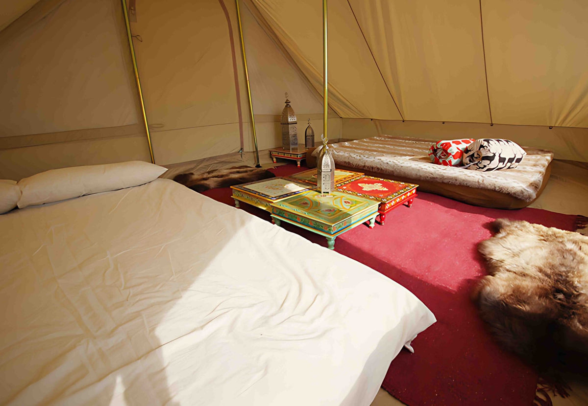 CanvasCamp Roman Traveller eingerichtet mit Bett, rotem Teppich und niedrigen bunten Tischchen