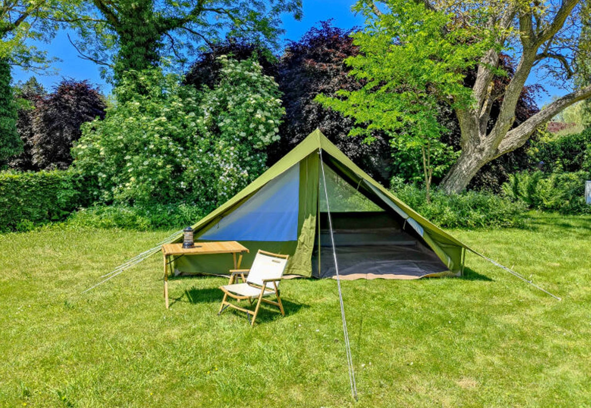 CanvasCamp Patrol Pro mit Klapptisch und Stuhl vor dem offenen Zelt in einem sonnigen Garten