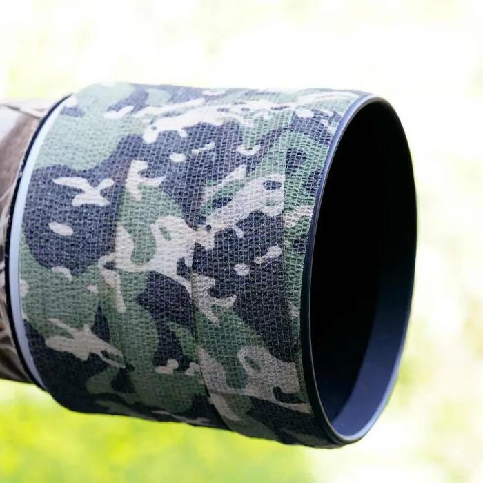 Stealth Gear Tarnband um die Vorderseite eines Kameraobjektivs gewickelt, draußen im Grünen