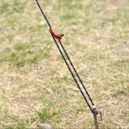 Winnerwell Guyline Peg Set, Abspannleine mit rotem Spanner an einem Hering im Gras