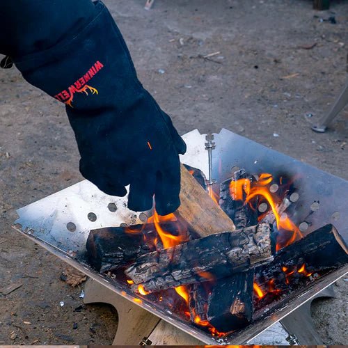 Winnerwell Handschuh im Einsatz, eine Hand legt Holz in eine brennende Feuerschale
