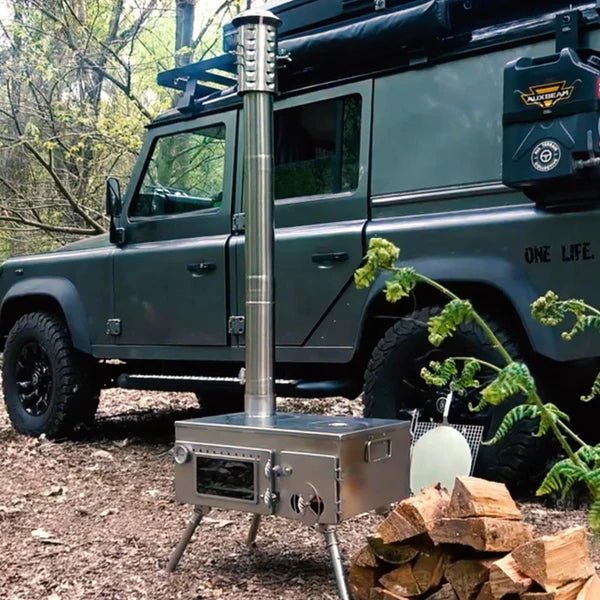 Winnerwell Woodlander Pizza Oven draußen im Wald vor einem Geländewagen, daneben Holz
